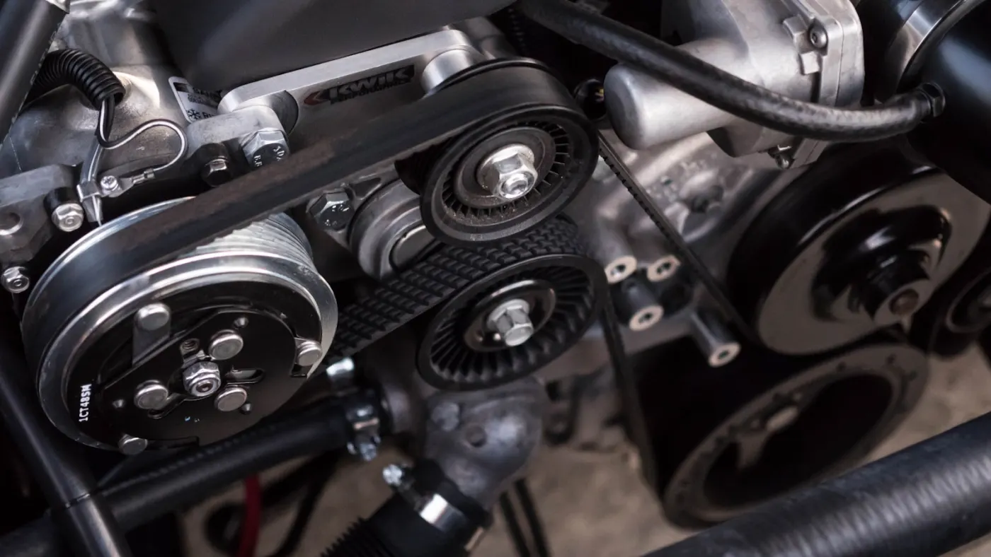 Close-up of an engine bay: serpentine belt, tensioner pulleys and the air conditioning compressor