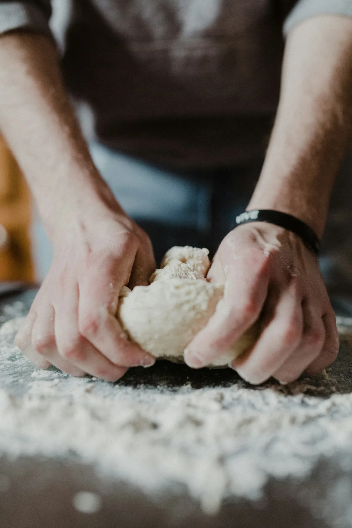 Two hands working a ball of dough on a floured bench