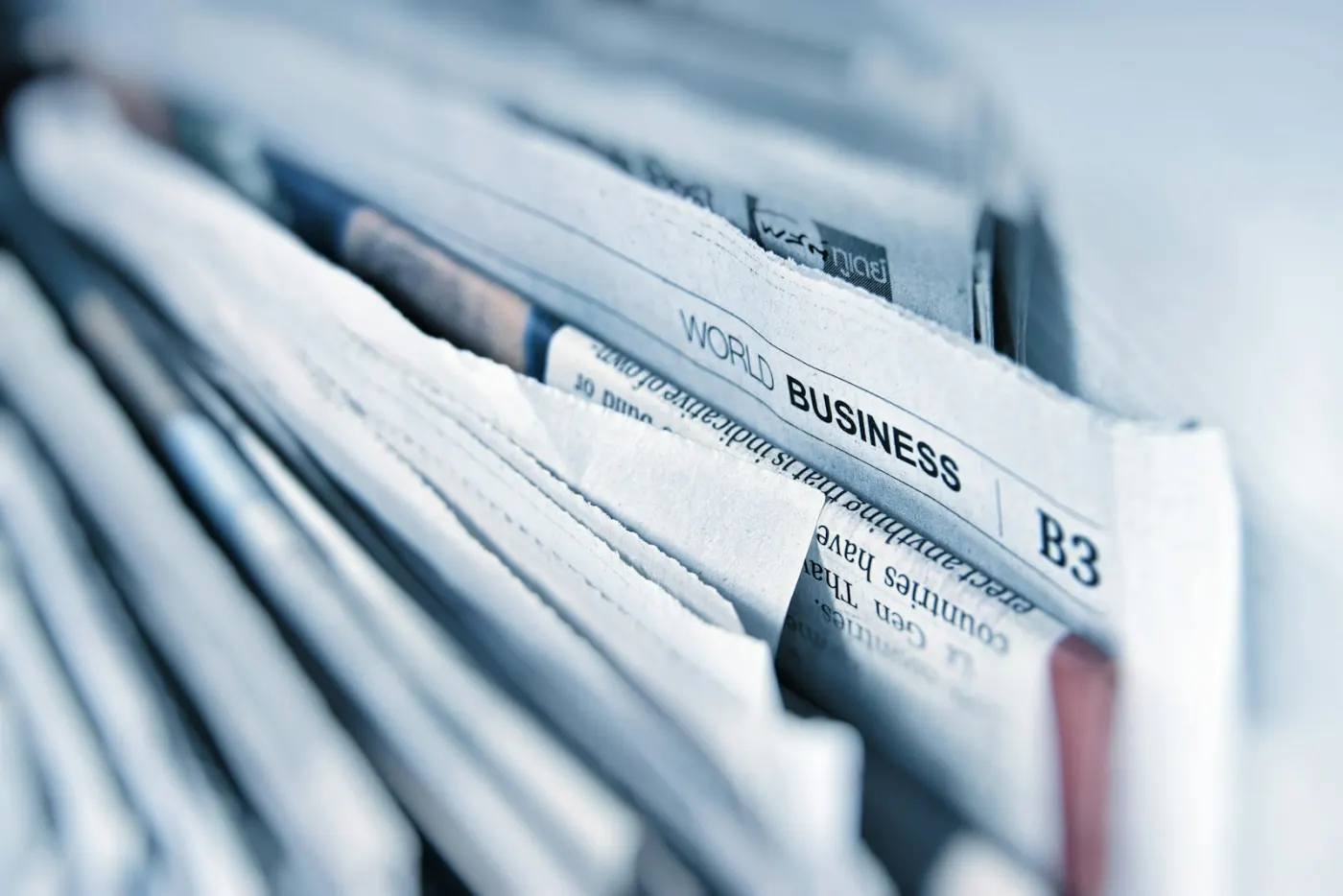 A stack of folded newspapers, the top one open at its business section