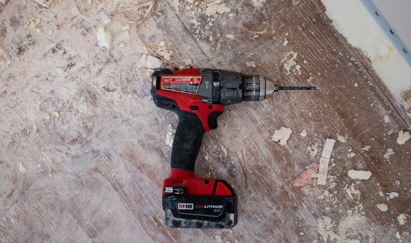 Cordless drill and drywall dust on a bare subfloor partway through a job