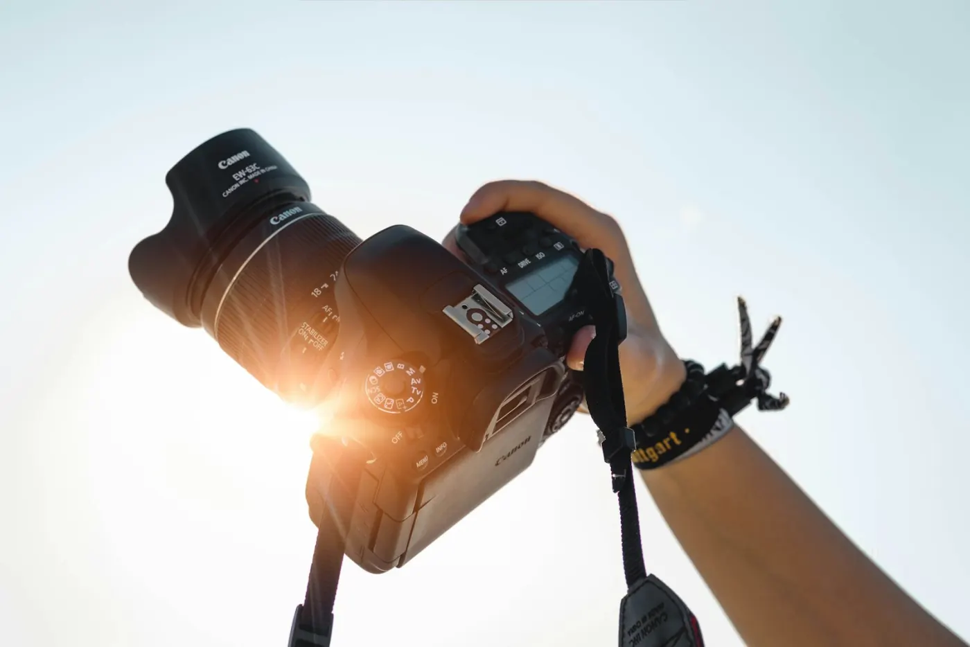 A hand holding a camera up against a bright sky